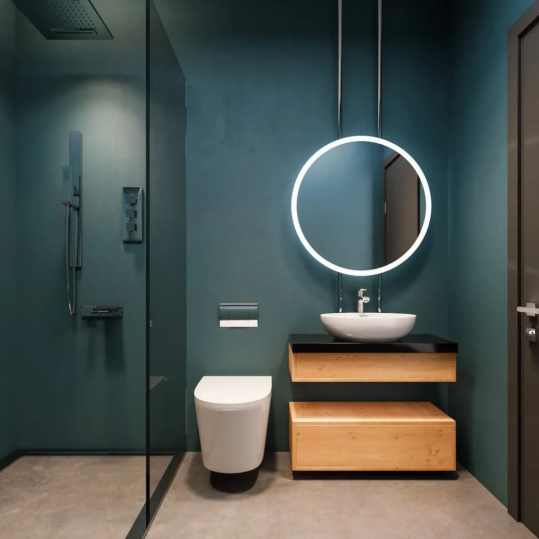 Koupelna se svítícím kulatým zrcadlem a stěnou v barvě námořnické modré mikrocementu