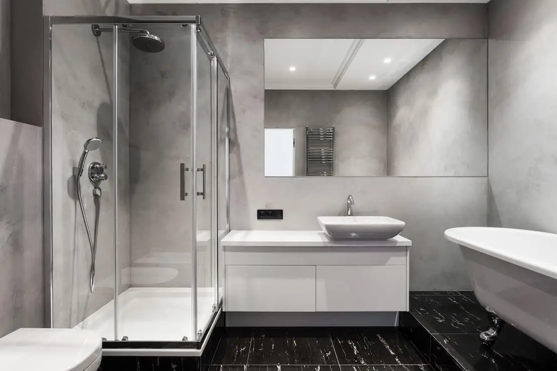 Kylpyhuone, jossa on valkoiset kalusteet ja seinä harmaalla mikrosementin värillä