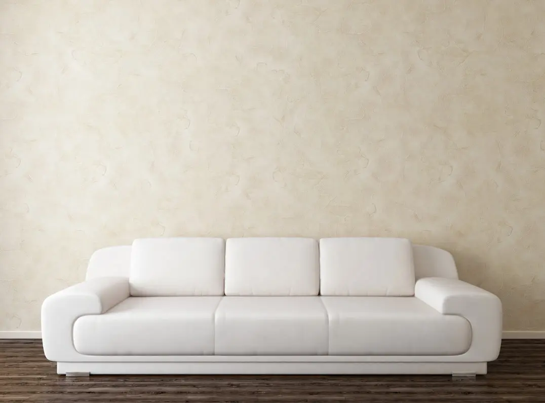Aplikacja weneckiego tynku na ścianie w neutralnych kolorach, które doskonale komponują się z skórzanym fotelem i drewnianą podłogą